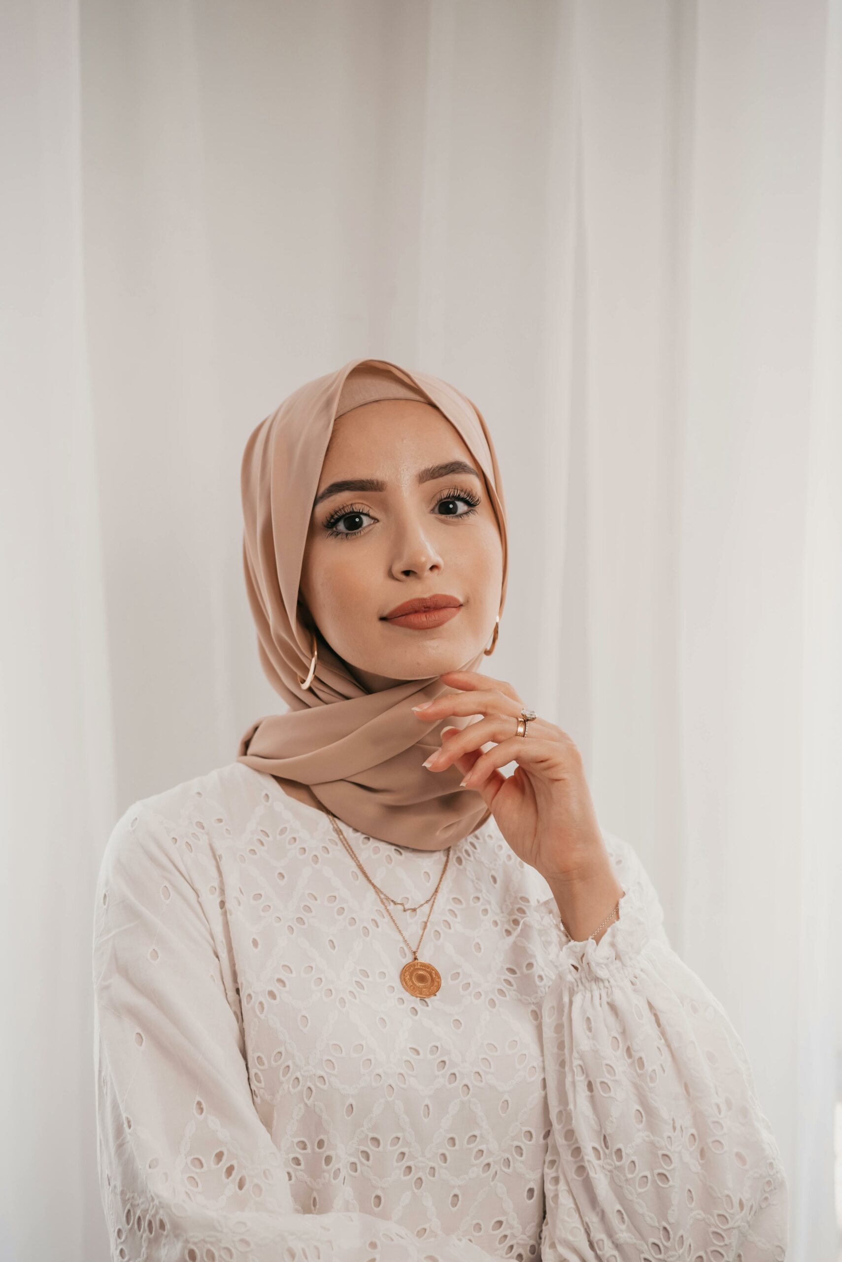Studio shot of a beautiful woman wearing a hijab and white lace dress, exuding elegance and grace.